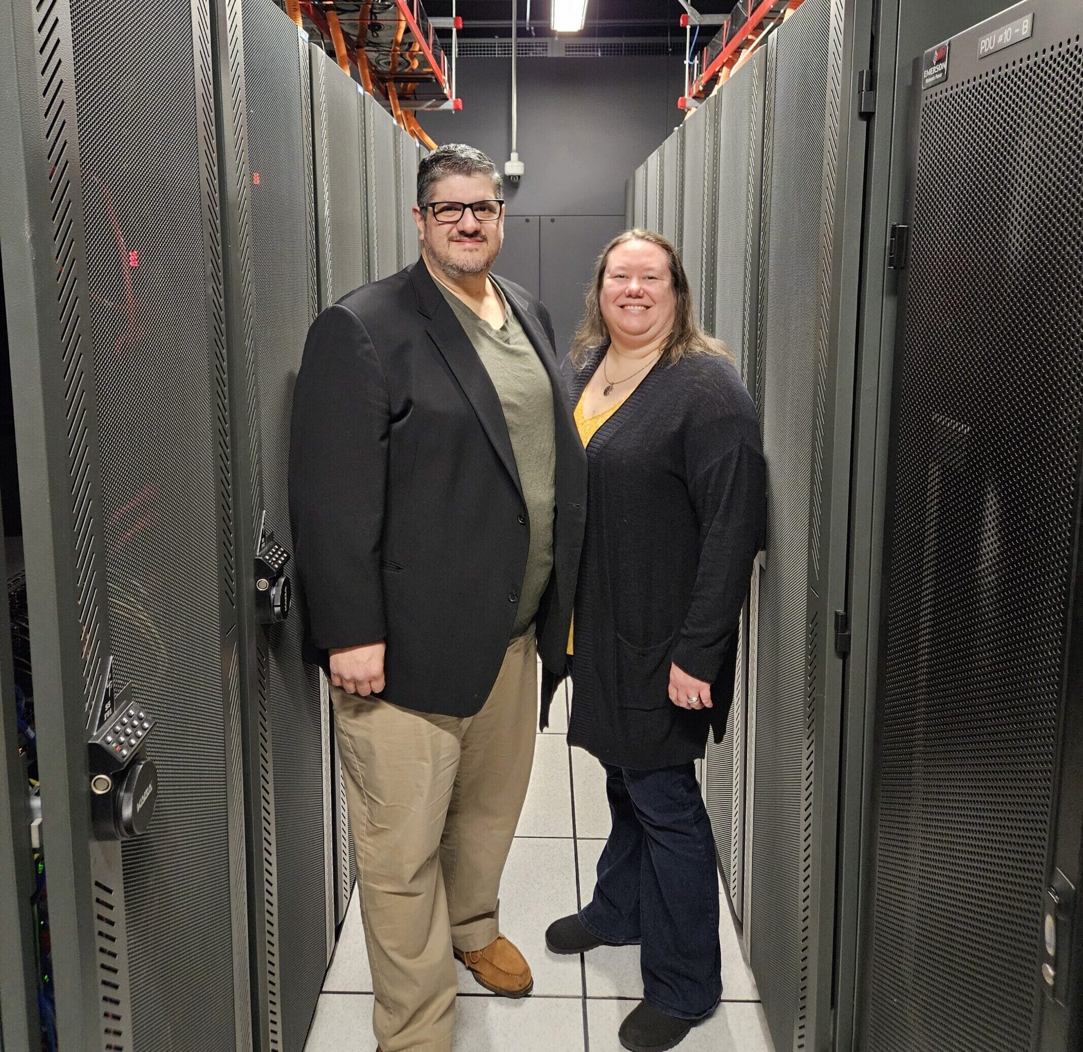 Tony and Rebekka Sollars stand in an aisleway of a server room.
