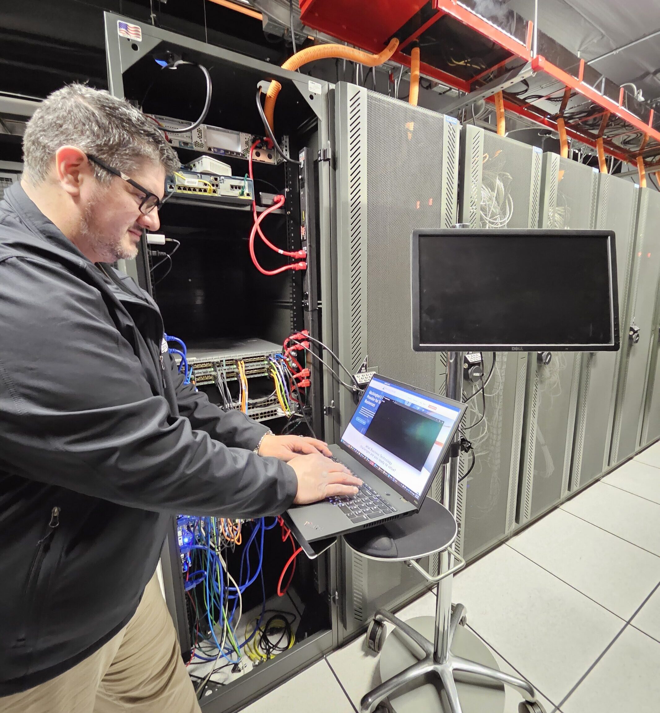 An IT expert works from his laptop in a server room.